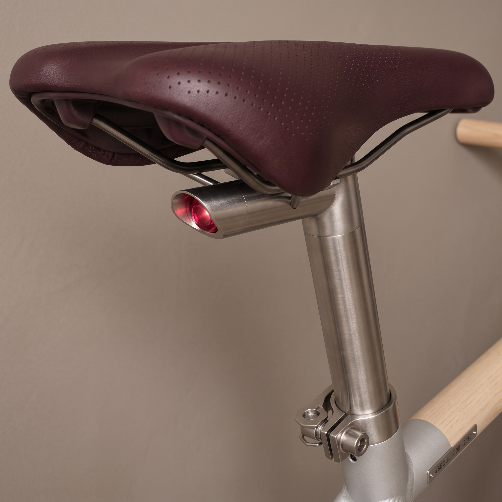 Detail of the perforated burgundy leather saddle, brushed stainless steel seatpost with integrated rear red LED light, and engraved serial plaque