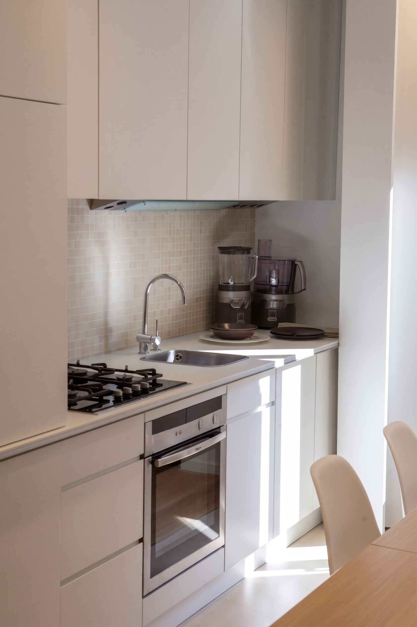 Linear minimalist kitchen with white handleless cabinetry, stainless steel finishes, and mosaic tile backsplash